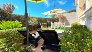 Un espace extérieur aménagé en terrasse, avec deux chaises longues, une table et un parasol jaune.