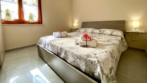 Un lit bien fait, recouvert d’une couvre-lit à motifs, avec deux lampes de chevet et des serviettes ornées de rubans rouges.