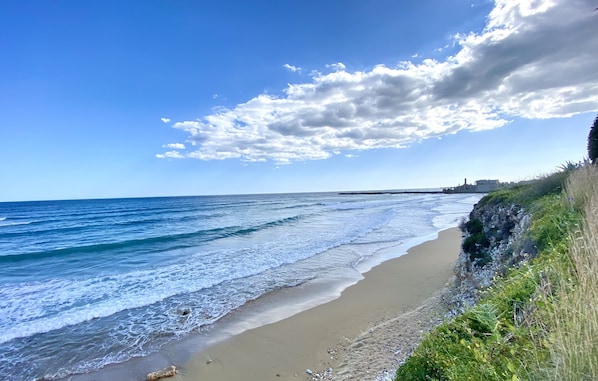 A beach with waves, a clear sky, and a distant building.