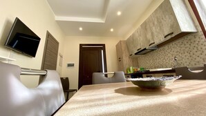 Un coin repas avec une table, des chaises, un téléviseur fixé au mur et une cuisine en arrière-plan.