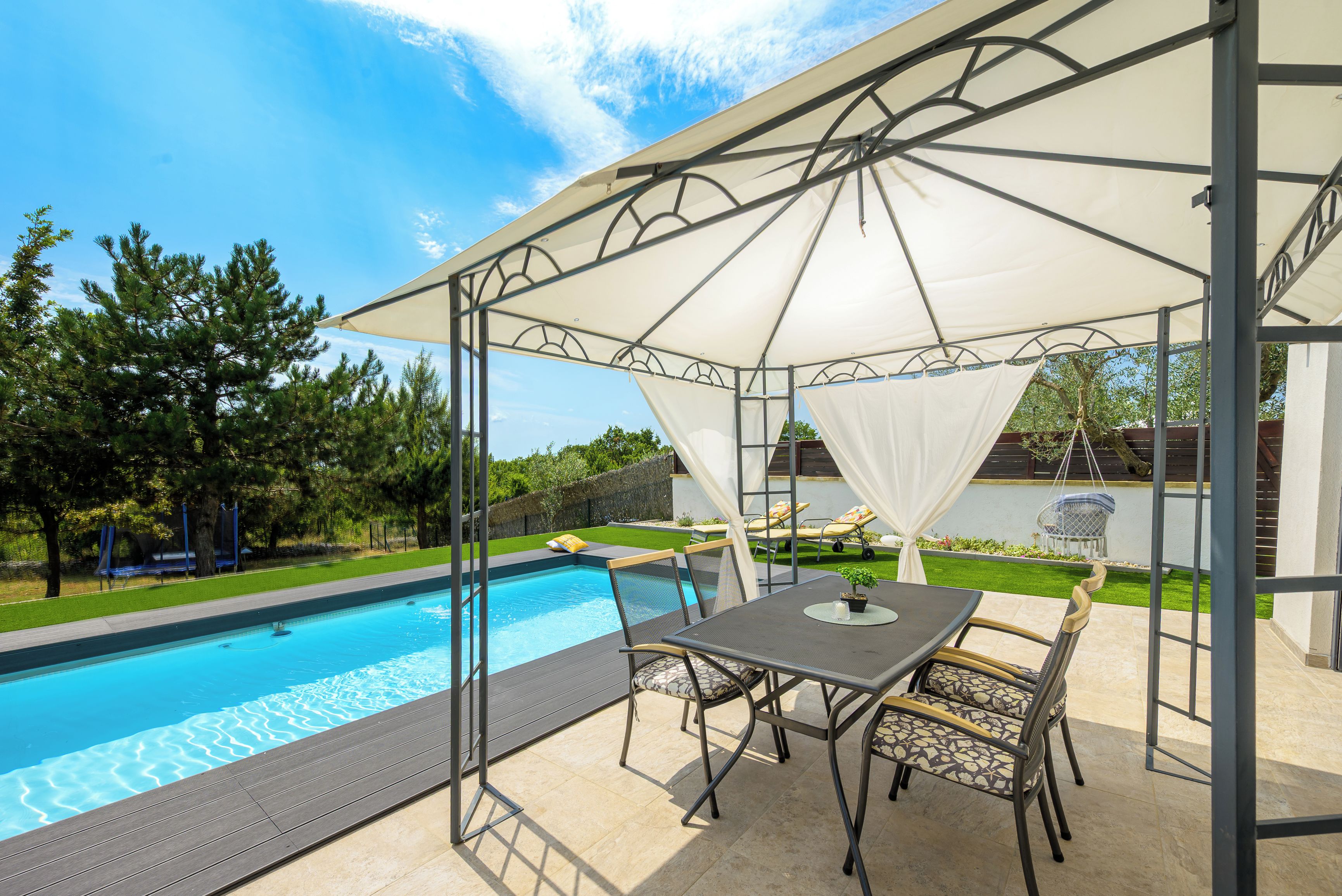 A covered outdoor seating area with a pool, chairs, and a table.