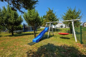 Une aire de jeux avec un toboggan bleu, une balançoire et un trampoline.