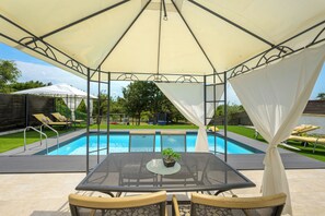Un espace extérieur abrité comprenant une piscine, des chaises longues et une table avec des chaises.