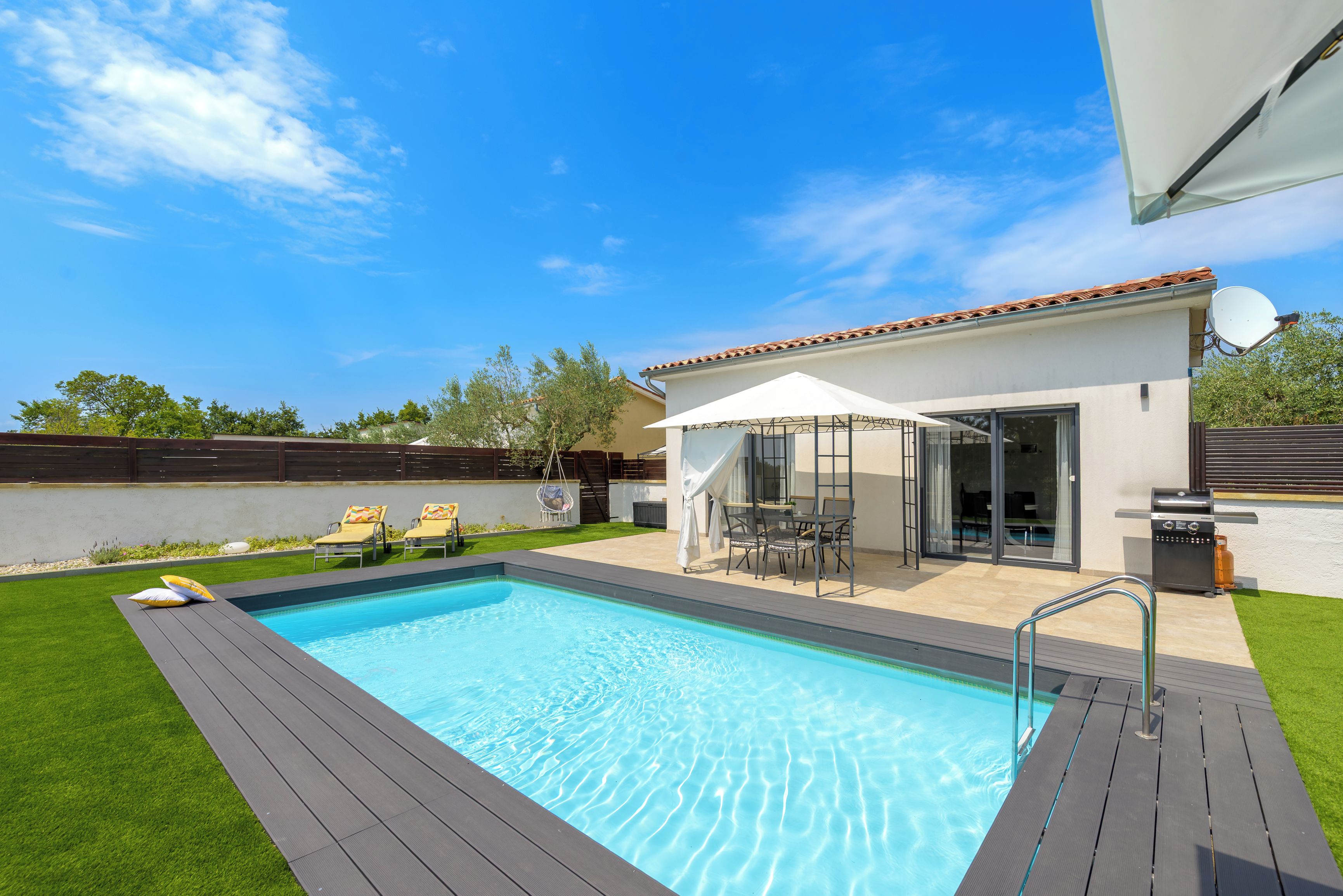 A swimming pool with a deck, a covered patio area with outdoor furniture, and a view of the sky.