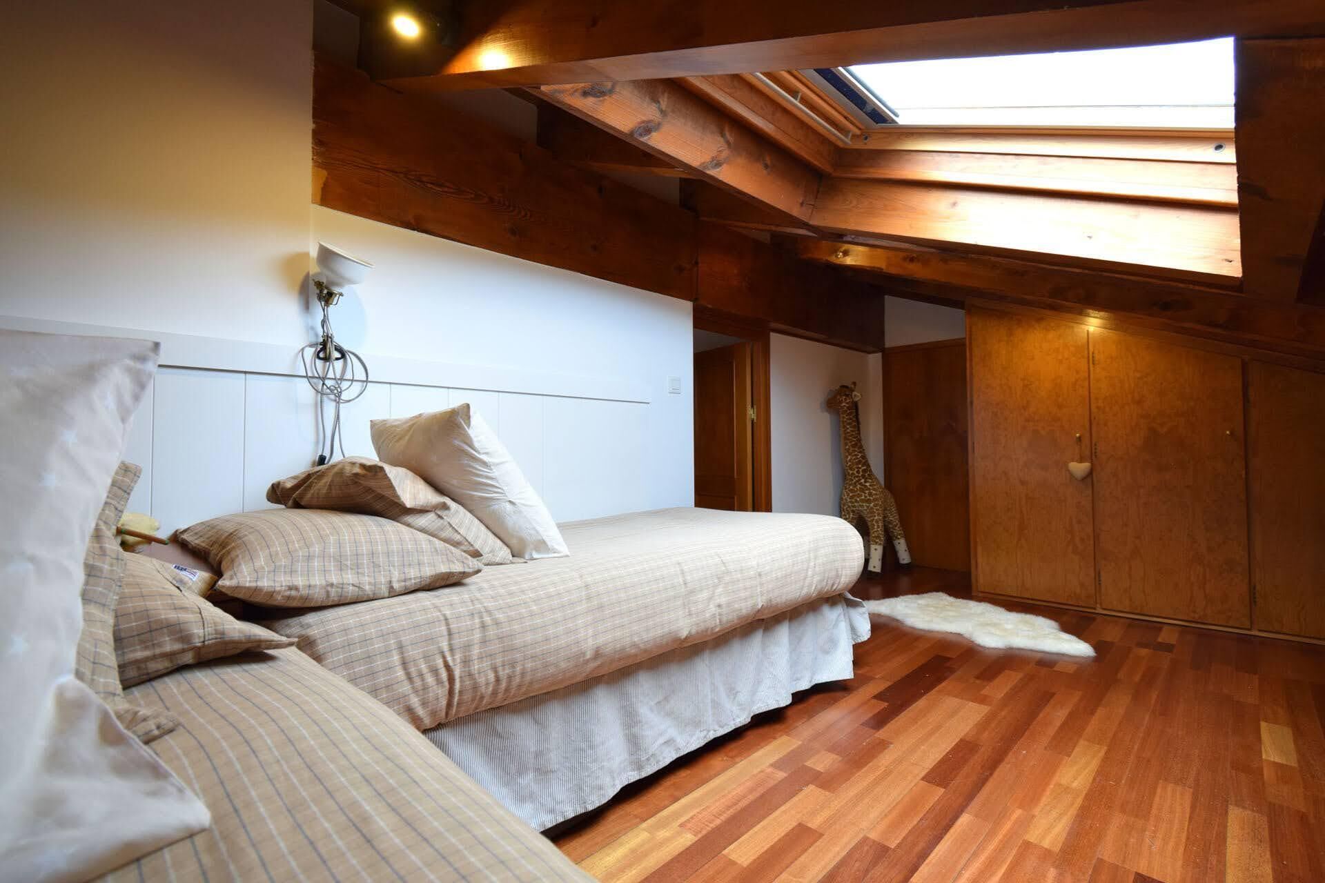 Une chambre avec une lucarne, des poutres en bois, un lit avec de nombreux oreillers et une décoration sur le thème des girafes.