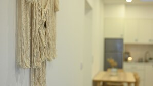 A room with a macrame wall hanging, a wooden dining table, and a kitchen area in the background. - Casa do Porto, relax with this stunning sea view (Porto Formoso)