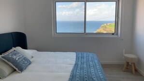 A bedroom with a bed, a window with a view of the sea, and a small stool. - Casa do Porto, relax with this stunning sea view (Porto Formoso)