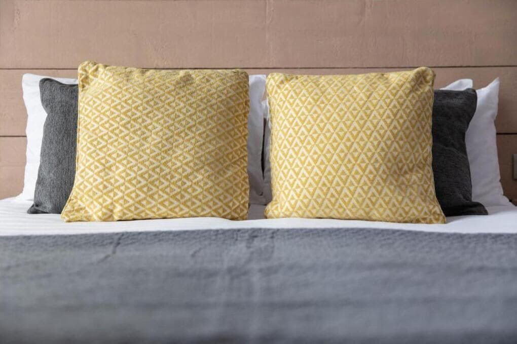 A bed with two pillows, one yellow and one gray, and a gray blanket.