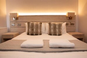 A neatly made bed with two fluffy pillows, a bedside table with a lamp, and a wall-mounted light fixture. - The Vanguard - York Residence (York)
