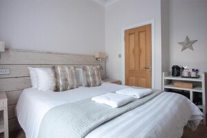 A neatly made bed with white bedding and a grey throw blanket, a wooden headboard, a bedside table with a lamp, and a star decoration on the wall.