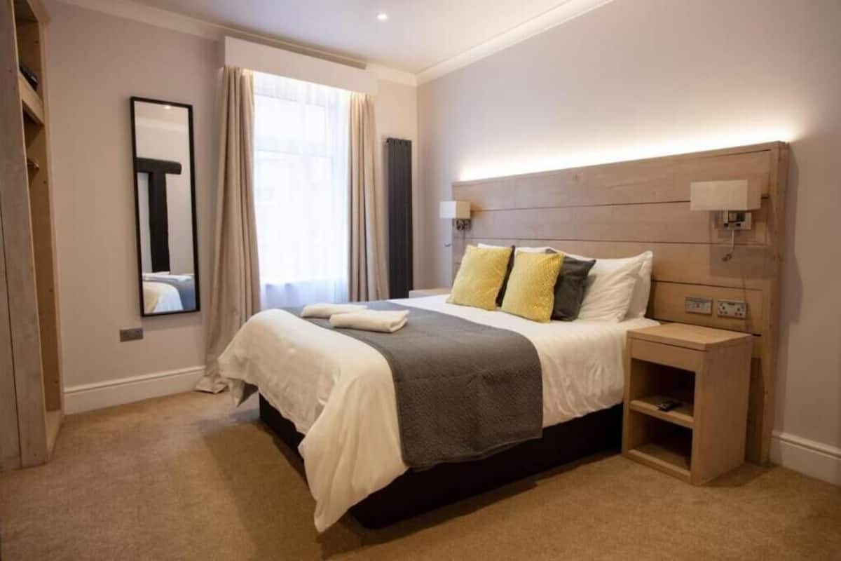 A neatly arranged bedroom with a large bed, bedside lamps, and a mirror.