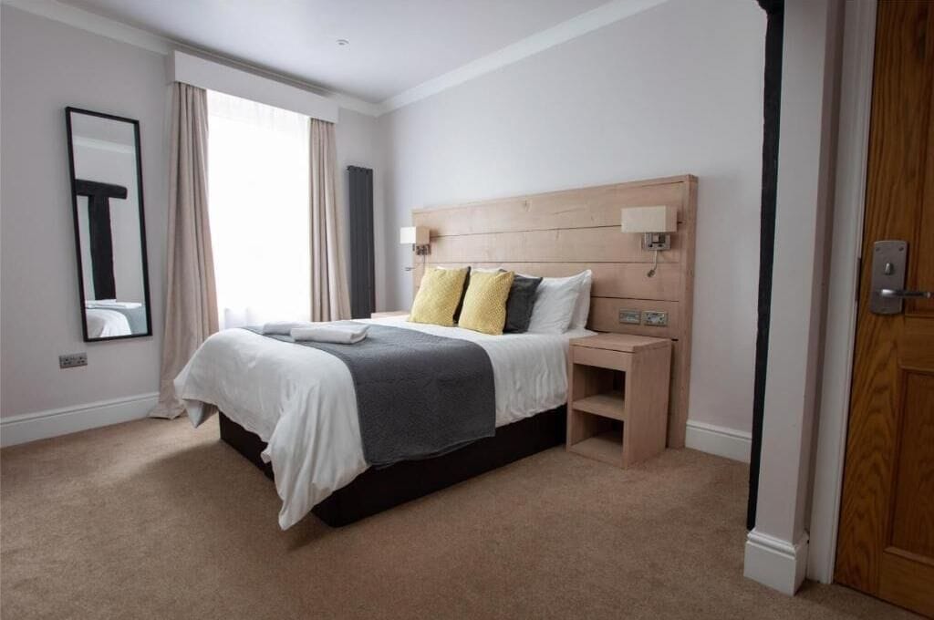 A hotel room with a large bed, bedside tables, a mirror, and a wooden headboard.