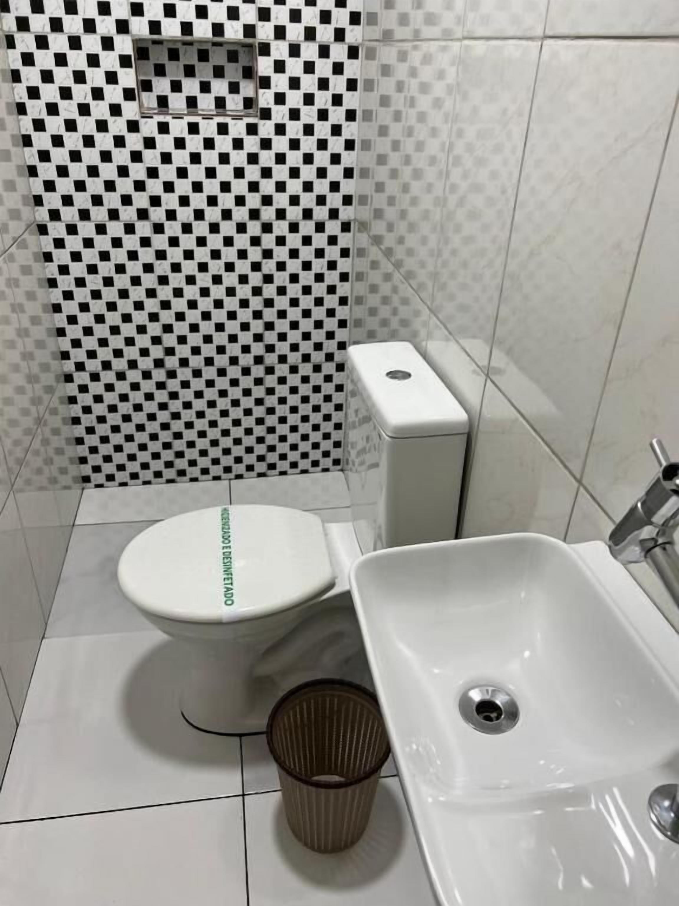 A bathroom with a toilet, sink, and trash bin.