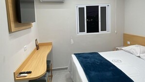 A modern hotel room with a bed, a desk with chairs, a TV, and an air conditioning unit. - Hotel Ellos (Itaquaquecetuba)