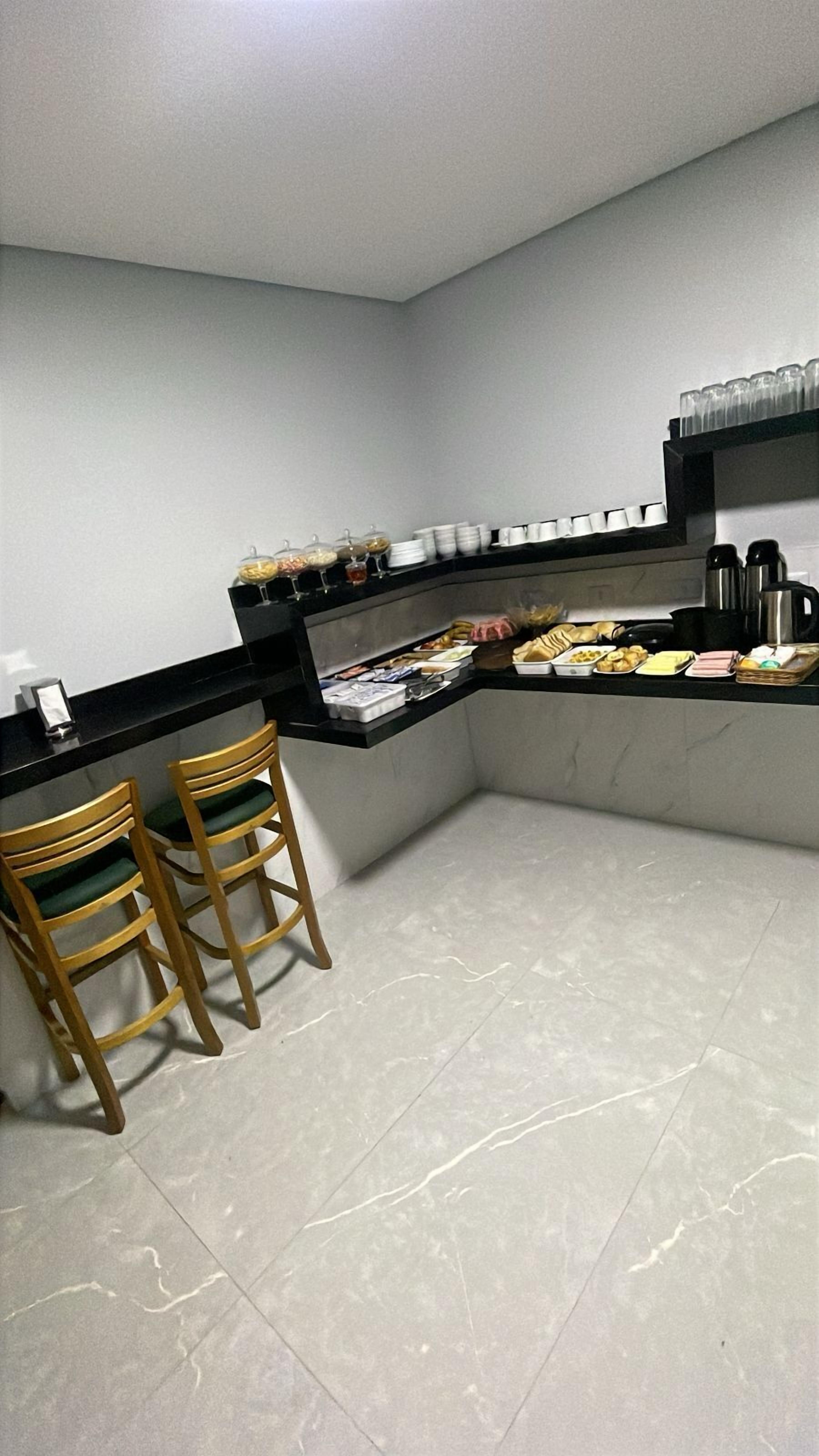 Uma pequena cozinha com bancada, duas cadeiras de madeira e diversos alimentos e utensílios.