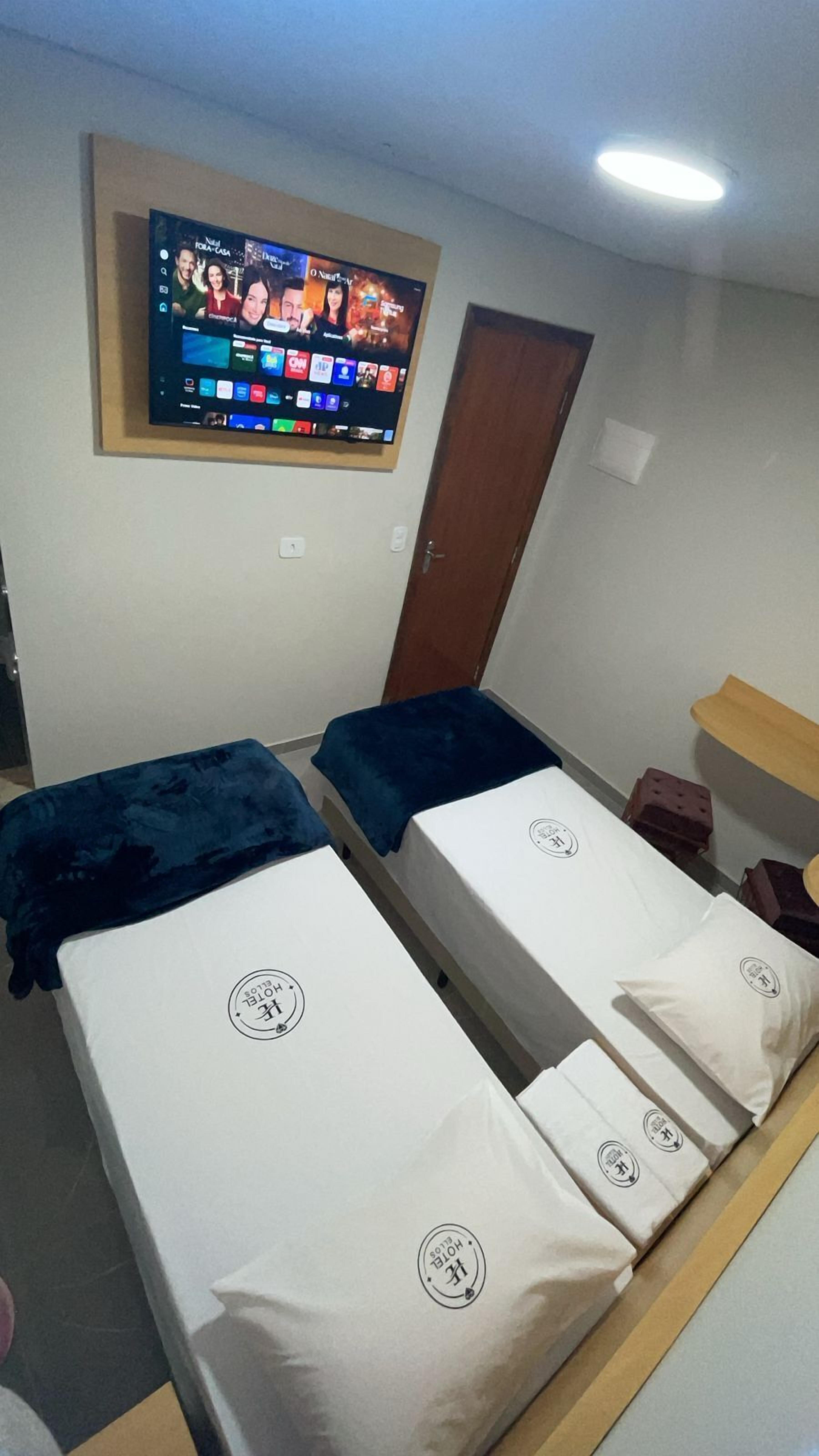 Habitación de hotel con dos camas individuales, un televisor montado en la pared y un cabecero de madera.