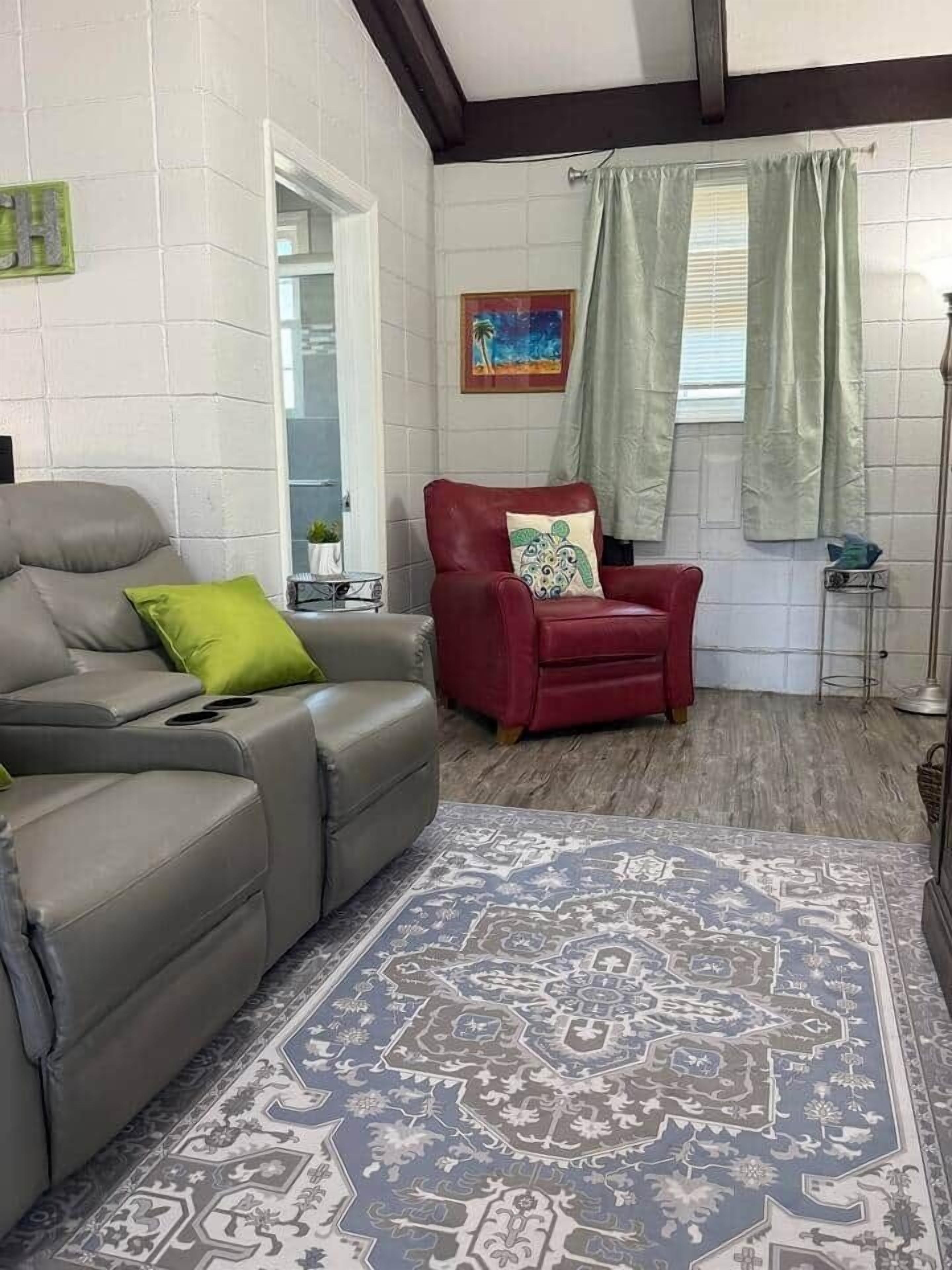 A living room with a grey sofa, a red armchair, a patterned rug, and a painting on the wall.
