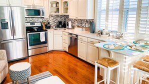 Una cocina moderna con armarios blancos, electrodomésticos de acero inoxidable, salpicadero de azulejos y una zona de bar con taburetes.