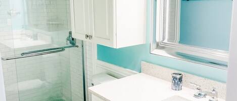 A bathroom with a toilet, a sink, a mirror, and a shower area.