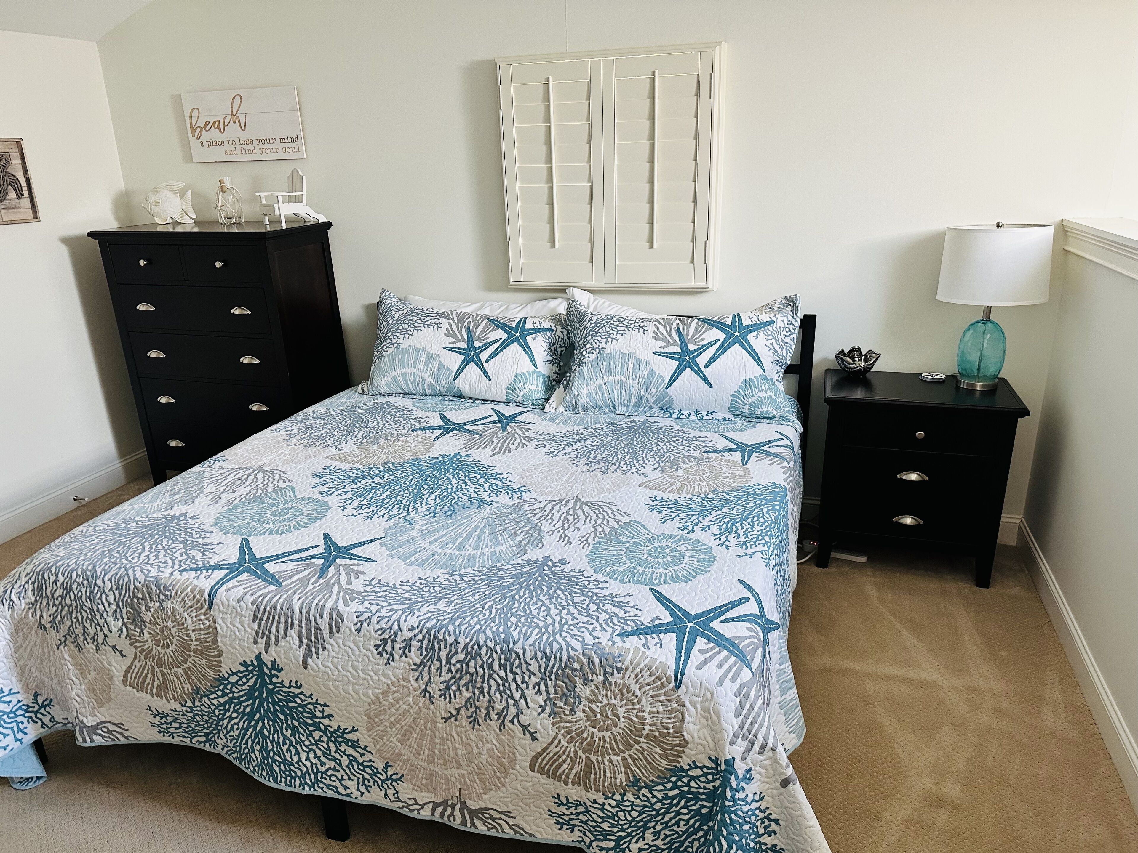 Une chambre à coucher comprenant un lit, une commode, une table de chevet, une lampe et un élément décoratif mural.