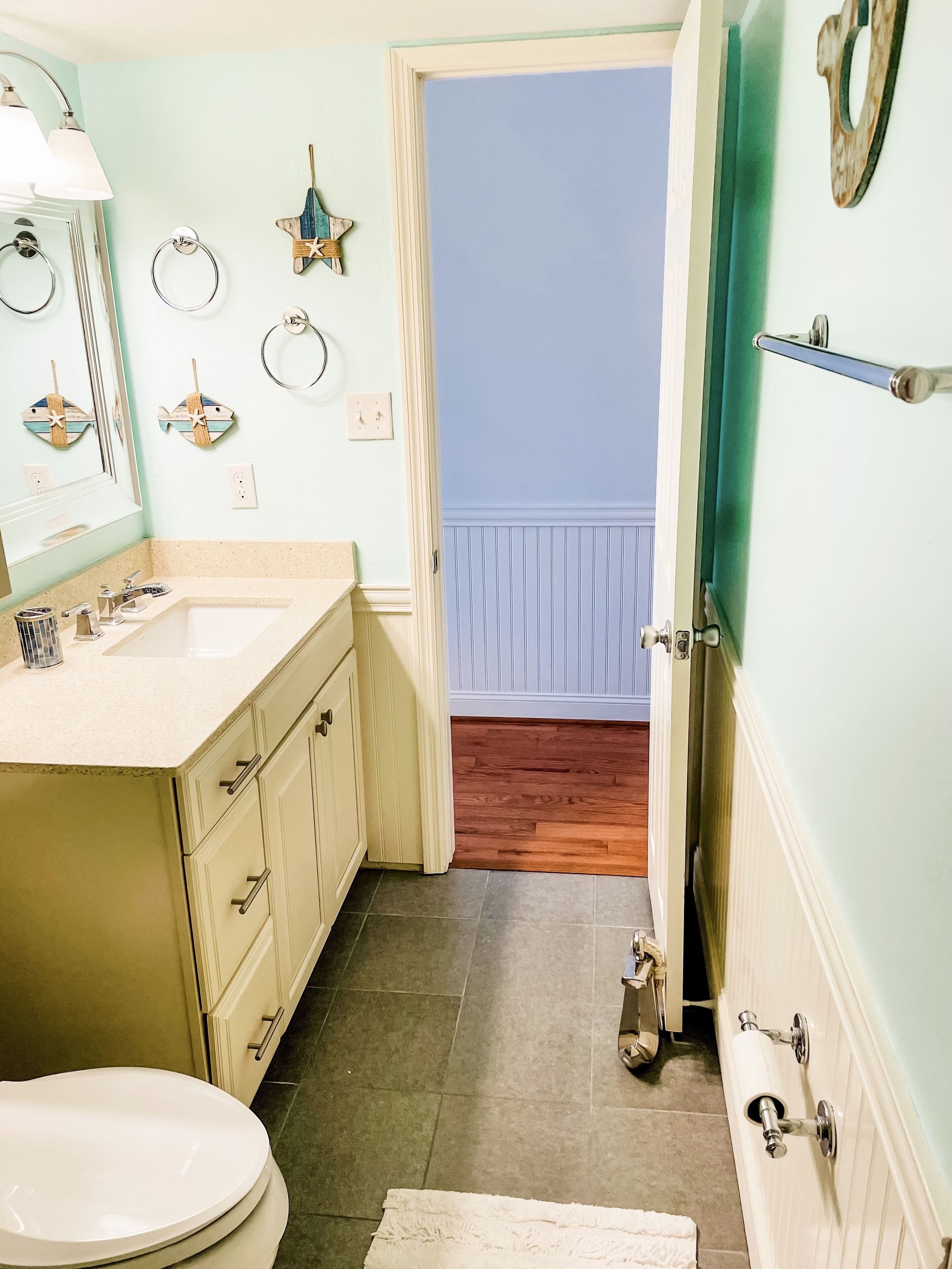 A bathroom with a sink, mirror, and toilet. There are decorative items on the wall and a towel rack.