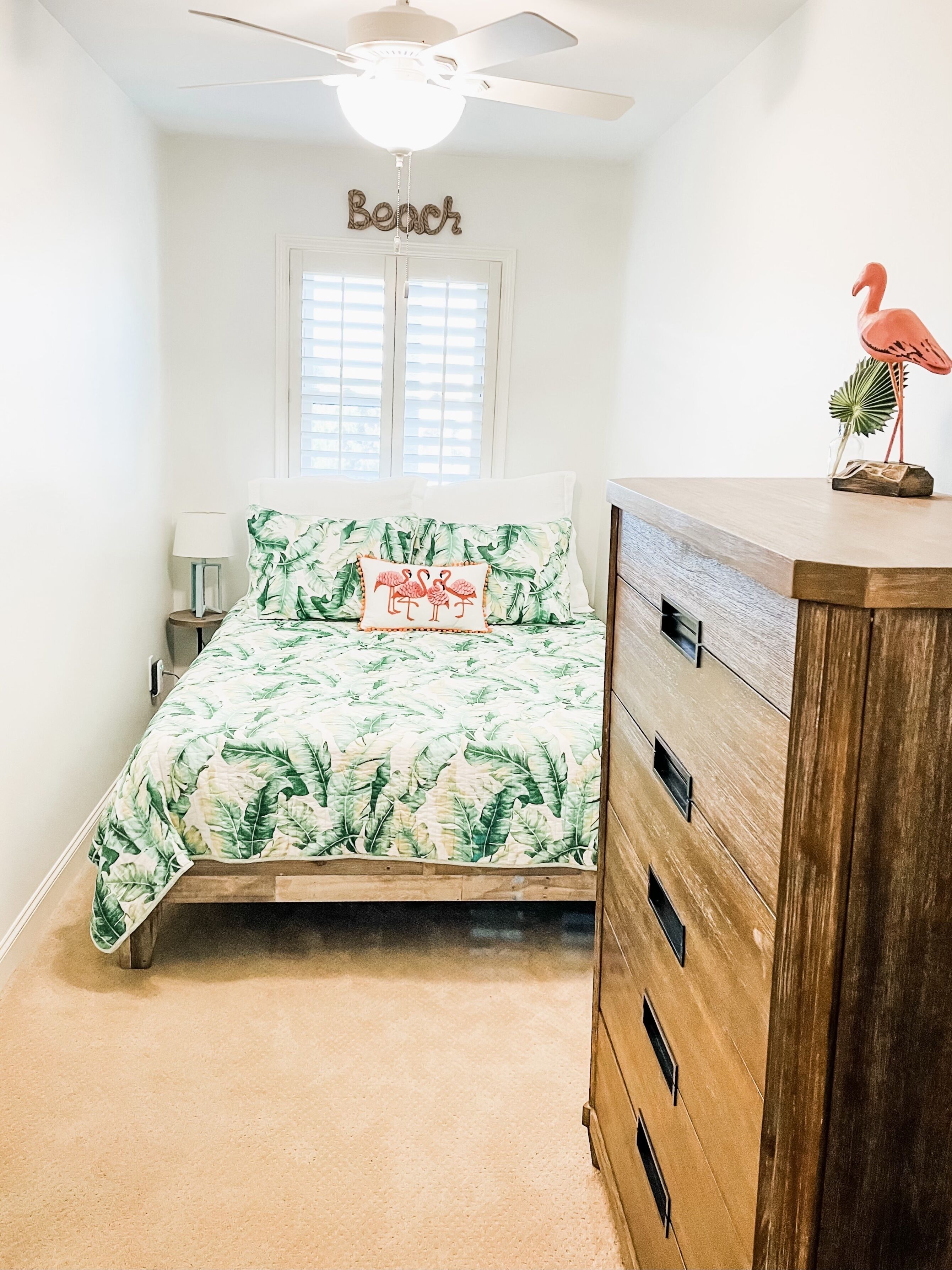 Ein Schlafzimmer mit Bett, Kommode, Deckenventilator, Fenster mit Jalousien und Wanddekoration.