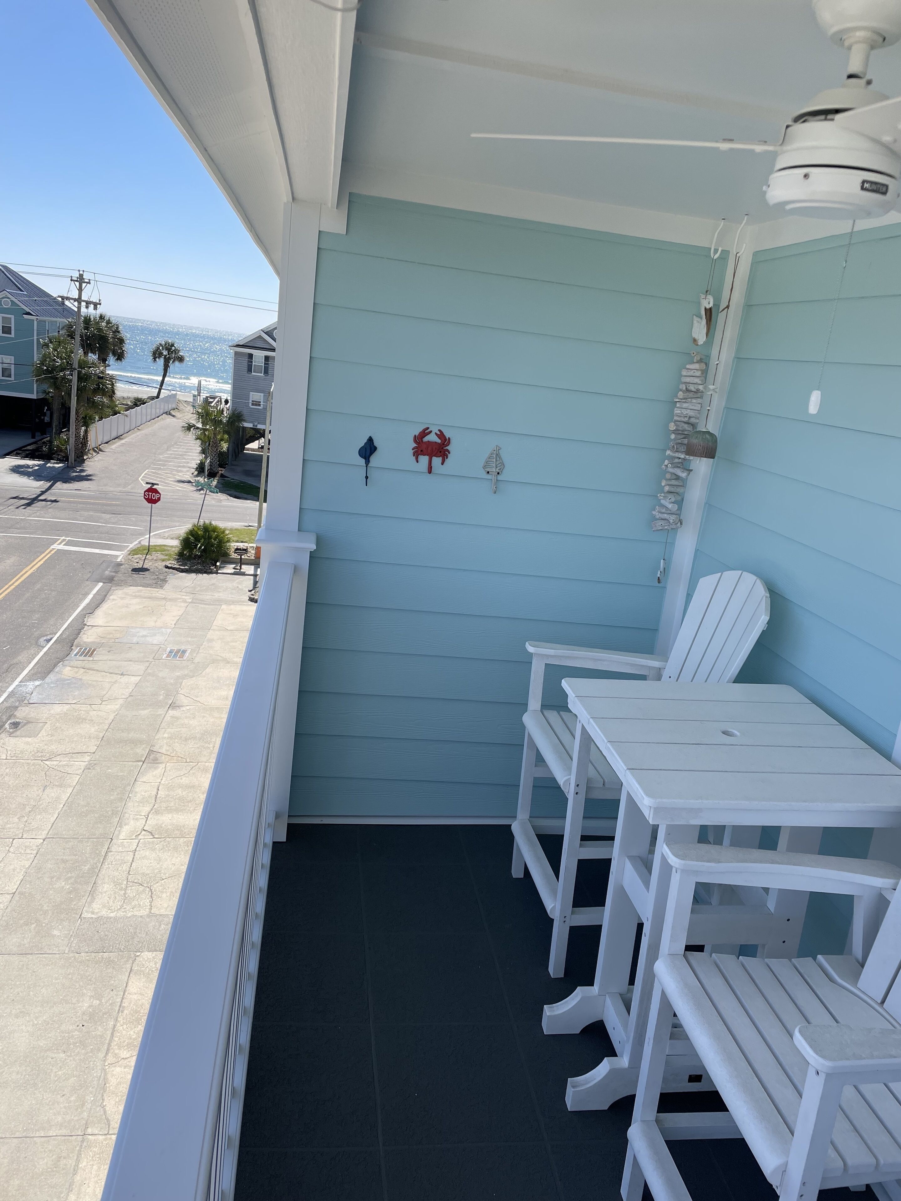 A balcony with a view of the street and ocean, featuring a stop sign, a red crab decoration, and a white table with chairs.