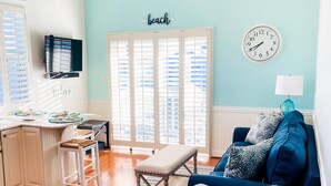 Una sala de estar con un sofá azul, un banco y un televisor en la pared.