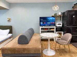 Una sala de estar moderna con un sofá, una mesa redonda, una silla, un televisor y un refrigerador.