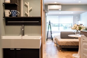 Un baño moderno con un lavamanos blanco, un espejo encima y una repisa con una taza azul y una taza blanca.