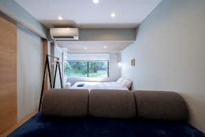 A narrow room with a bed, a window, and a hanging light fixture.