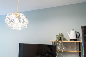 Una sala de estar moderna con un televisor de pantalla plana, una tetera blanca y una planta sobre una repisa de madera.