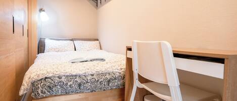A compact bedroom with a bed, a desk, and a chair.
