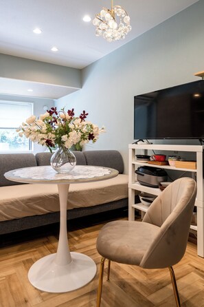A modern living room with a round white table, a beige armchair, a grey sofa, a flat-screen TV on a white stand, and a chandelier. - Akasaka Roppongi area with elevator Quiet high-class residential apartment close to train station (港区)