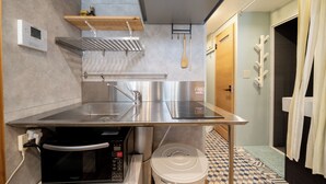 A compact kitchen with a stainless steel sink, microwave, and a small trash bin. There is a wooden shelf above the sink and a wooden spoon hanging on the wall. - Akasaka Roppongi area with elevator Quiet high-class residential apartment close to train station (港区)