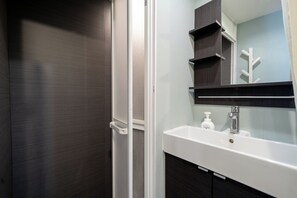 Un baño con lavamanos blanco, muebles de madera oscura y un espejo con repisa de madera encima.
