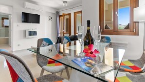 Un comedor moderno con una mesa de vidrio, sillas coloridas, una botella de vino y una revista.