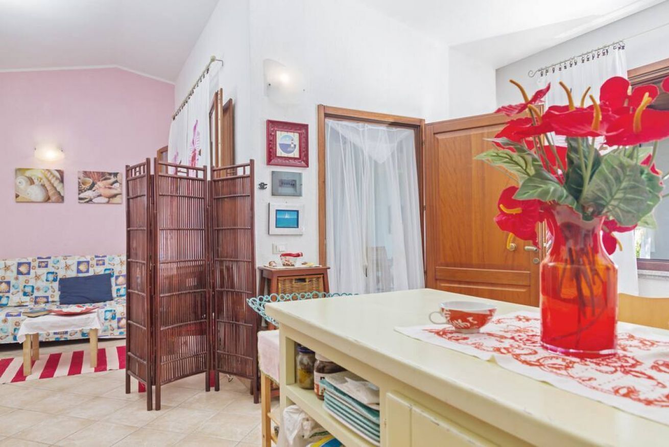 A room with a wooden partition, a dining table with a vase of flowers, and a sofa with a patterned cover.