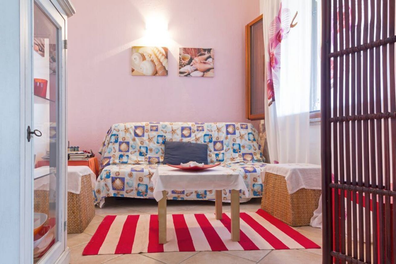 Um quarto acolhedor com sofá, uma mesa pequena, um tapete listrado em vermelho e branco, e um armário com portas de vidro.