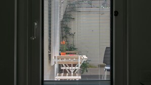 A view through a window with blinds, revealing a balcony with a table and chairs.