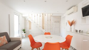 A modern kitchen with white cabinets, a dining table with orange chairs, and a staircase with a geometric railing.