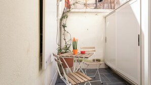 A small outdoor patio with a wooden table and chairs, a potted plant, and a white cabinet.