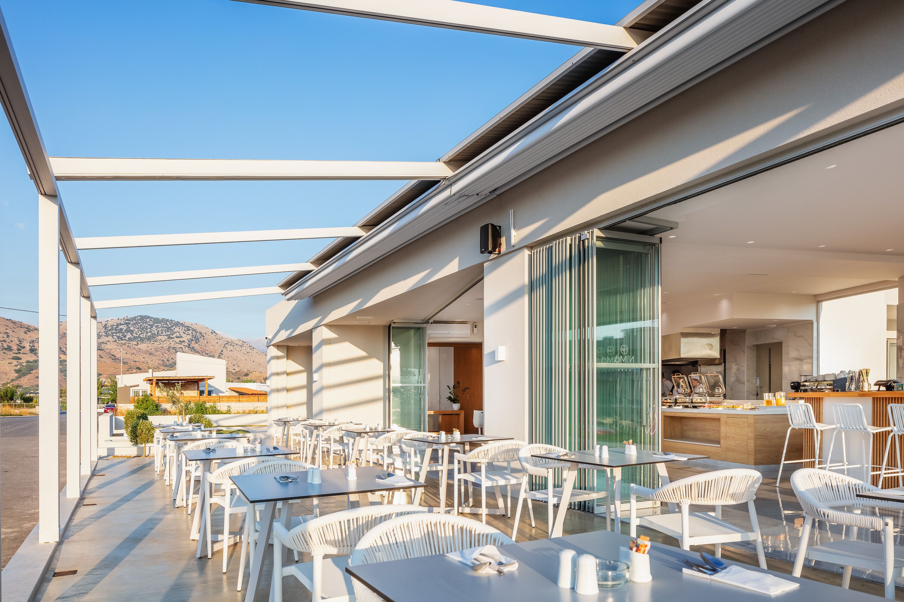 An outdoor seating area with white chairs and tables, a bar, and a view of mountains.