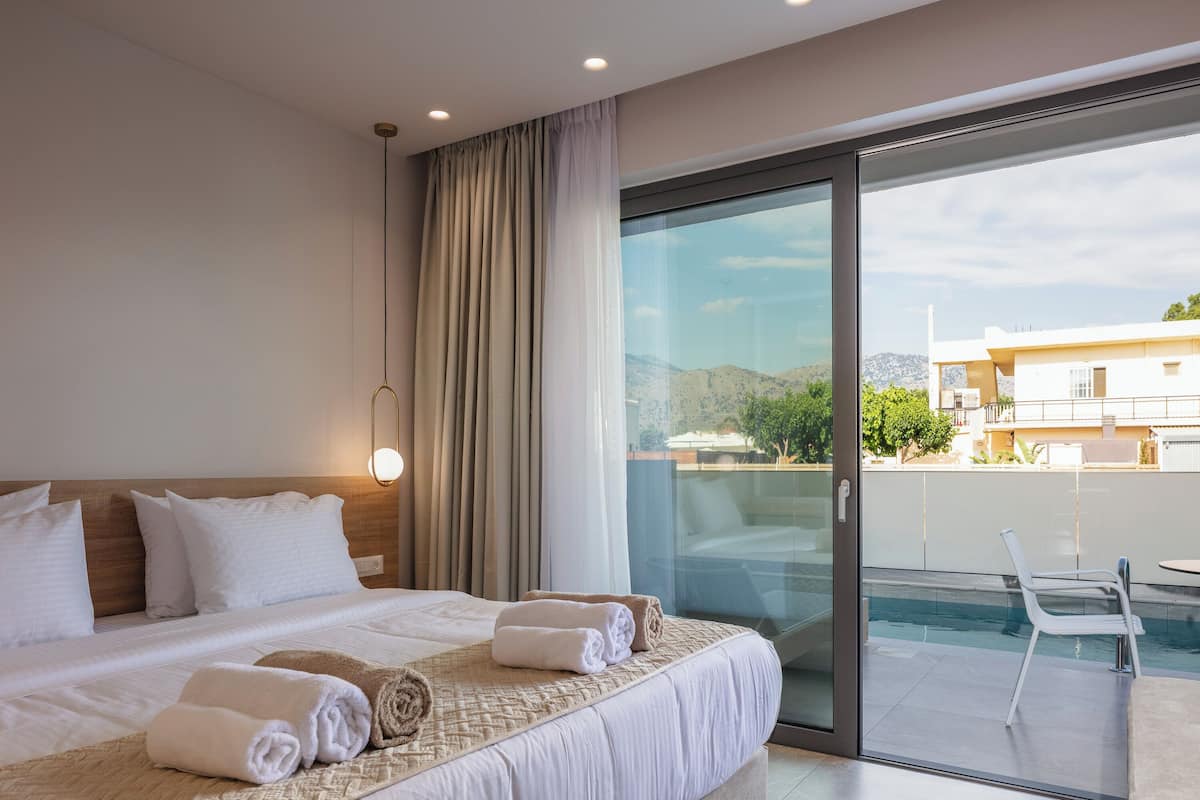 A hotel room with a large bed, a glass door leading to a balcony with a pool, and a view of the cityscape.