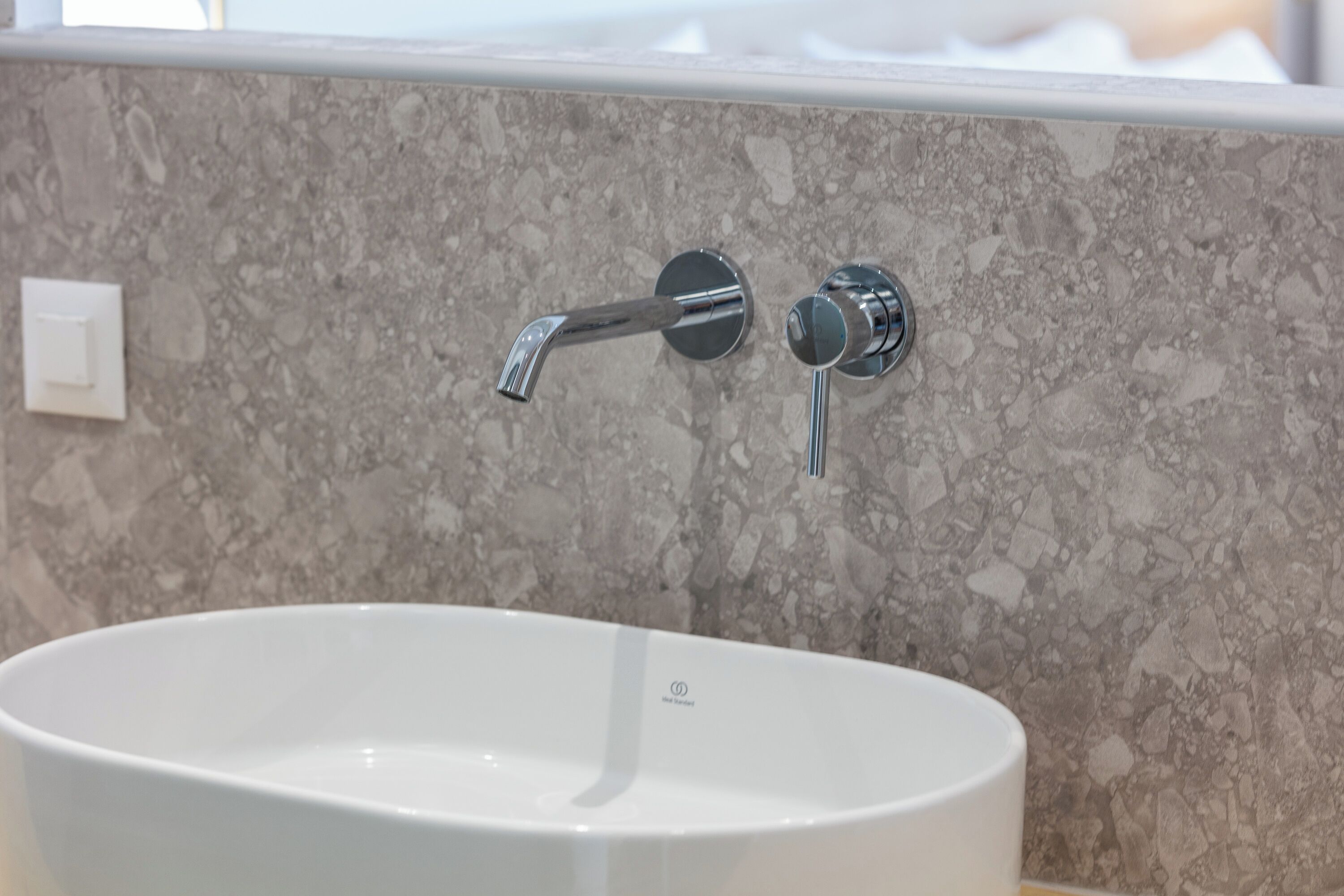 A bathroom with a white sink, a marble backsplash, and a chrome faucet.