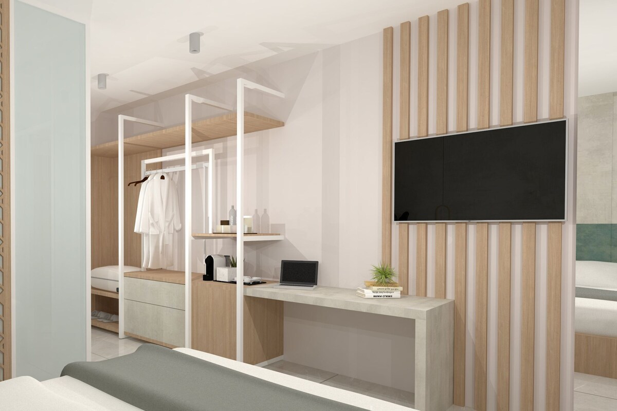 A modern bedroom with a bed, a desk, a TV, a wardrobe, and a plant.