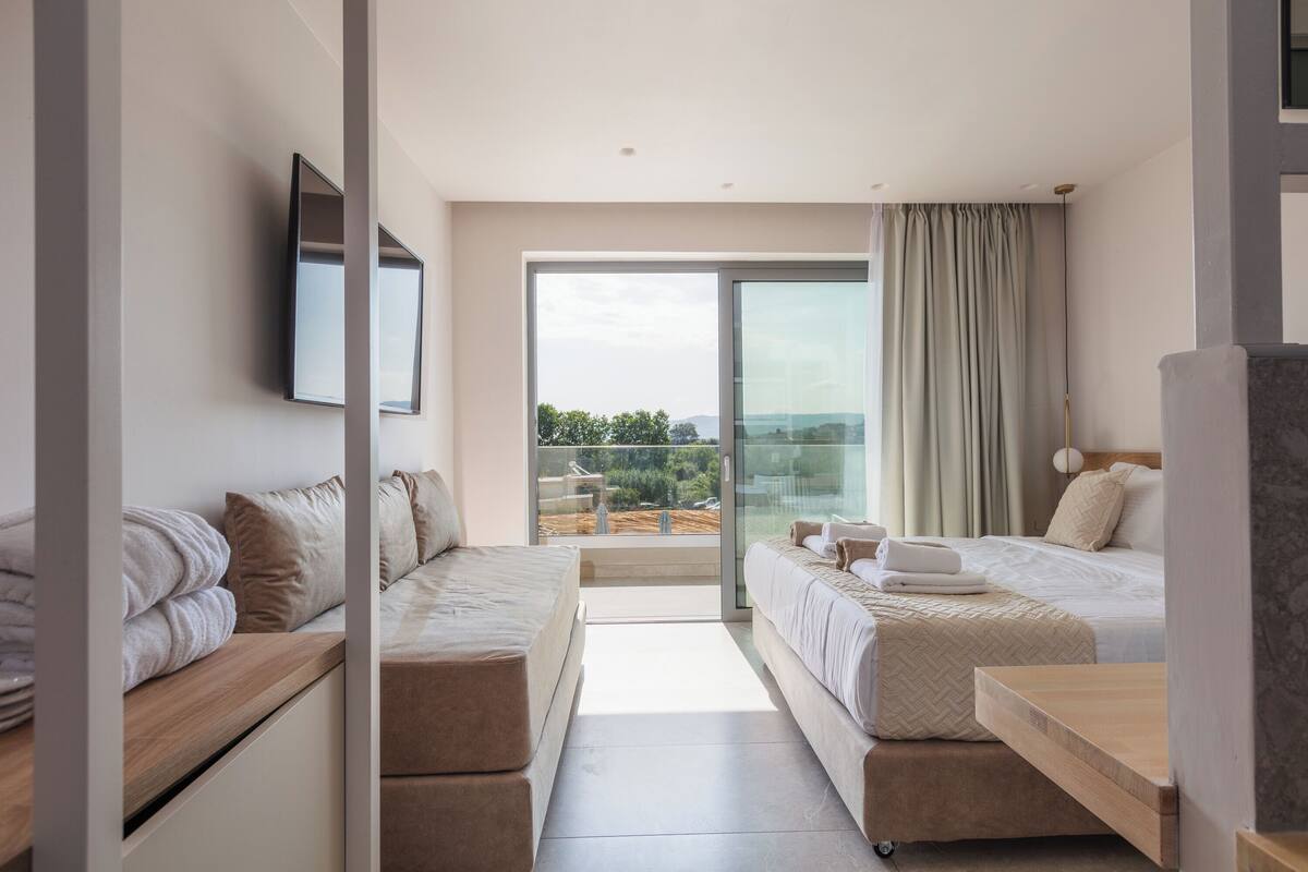 A modern hotel room with a large sliding glass door leading to a balcony, two beds, a flat-screen TV, and a minimalist design.