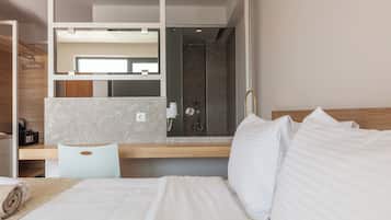 Una habitación de hotel moderna con cama, escritorio, silla, zona de ducha y un espejo grande.