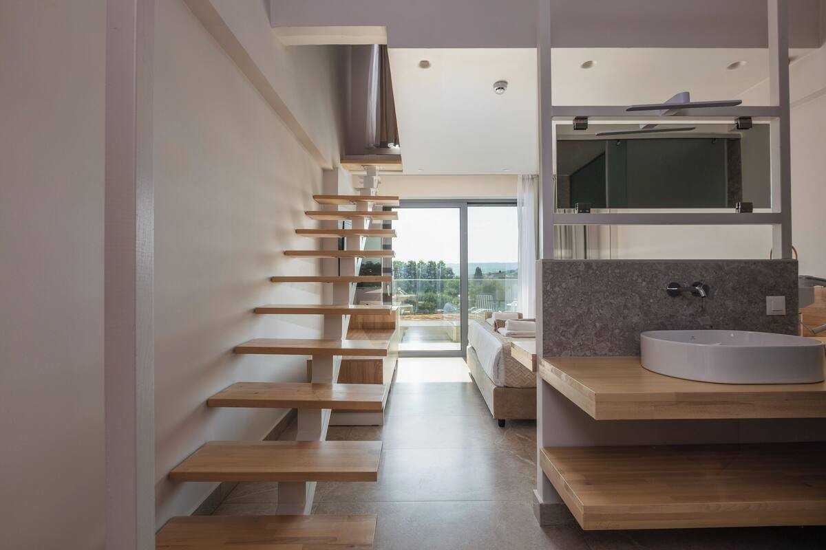 A modern bathroom with a wooden staircase, a large window, and a built-in sink.