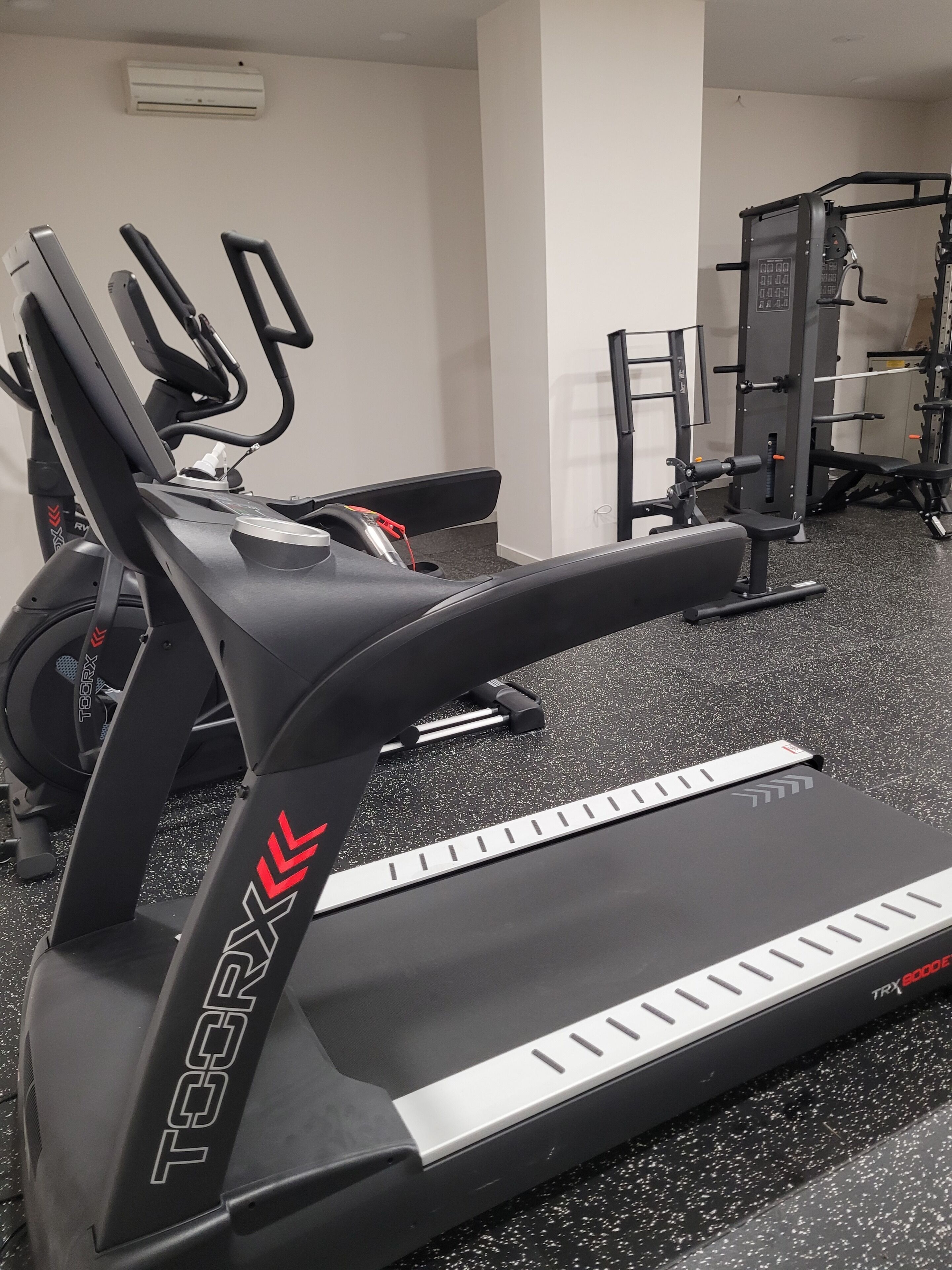 Un vélo d’appartement, un banc et un appareil de musculation dans une salle de sport.